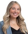 Headshot: Blonde woman in black top and med. blue jacket smiling at camera