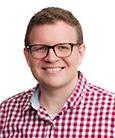 Headshot: Man in red and white with glasses smiling at camera